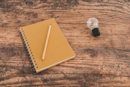 lightbulb metaphor of inventive ideas next to plain notebook and pencil on wooden office desk,...