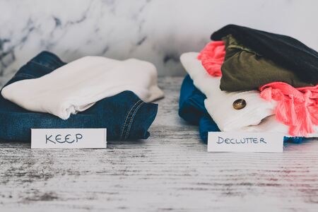 declutter and tidying up concept, fashion clothes folded and stacked into Keep and Declutter piles with text on paper labels in front of themの写真素材
