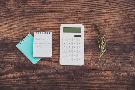 Company's Environmental Impact message on notead next to calculator and dry leaves, concept of...
