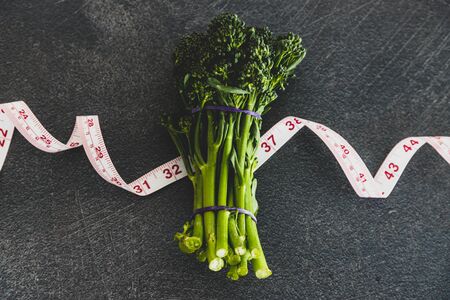 eating healthy and dieting concept, bunch of green organic broccolini on top of measuring tapeの写真素材
