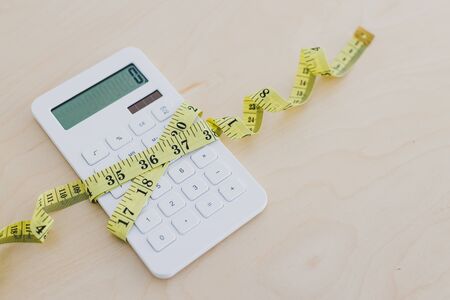 concept of tightening up your budget or expenses, calculator wrapped up by measuring tapeの写真素材