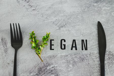 Vegan text with V made from small branches with leaves next to fork and knife, concept of healthy plant-based diet and animal rightsの写真素材