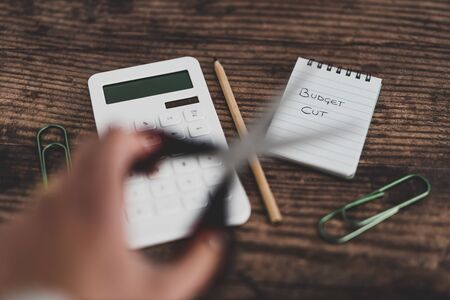 budget cuts conceptual still-life with text on notepad next to calculator and unfocused scissors in front of itの写真素材