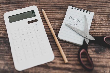 budget cuts conceptual still-life with text on notepad next to calculator and scissors on top of itの写真素材
