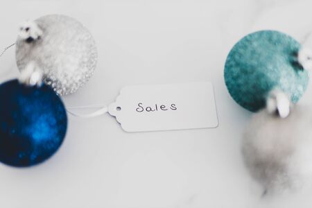festive season shopping and promotions conceptual still-life, Sales price tag with blue and silver Chirstmas baubles on marble desk shot at shallow depth of fieldの写真素材