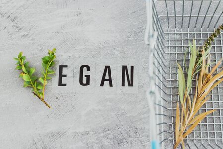 Vegan text with V made from small branches with leaves and shopping basket, concept of healthy plant-based diet and animal rightsの写真素材