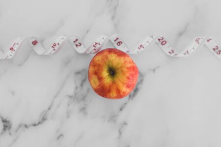 diet and nutrition concept, red apple with measuring tape on marble shot at shallow depth of fieldの写真素材