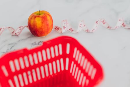 diet and nutrition concept, red apple with measuring tape and grocery store shopping basket shot at shallow depth of fieldの写真素材