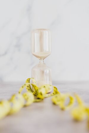being tight on time conceptual still-life, hourglass with measuring tape wrapped around it
