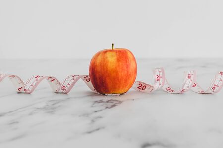 diet and nutrition concept, red apple with measuring tape on marble shot at shallow depth of fieldの写真素材
