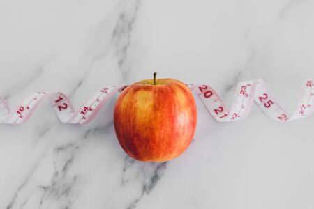 diet and nutrition concept, red apple with measuring tape on marble shot at shallow depth of fieldの写真素材