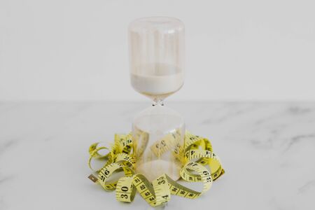 being tight on time conceptual still-life, hourglass with measuring tape wrapped around it