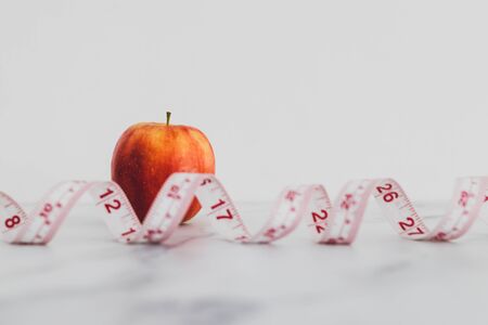 diet and nutrition concept, red apple with measuring tape on marble shot at shallow depth of fieldの写真素材