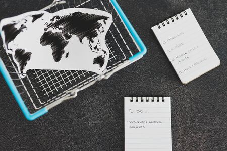 global business goals conceptual still-life, world map and shopping basket with Conquer Global Markets text on to do listの写真素材