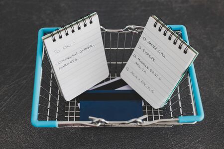 global business goals conceptual still-life, world map and payment cards inside shopping basket with Conquer Global Markets text on to do listの写真素材