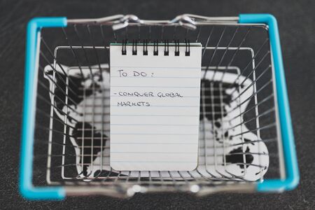 global business goals conceptual still-life, world map and shopping basket with Conquer Global Markets text on to do listの写真素材