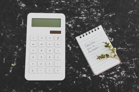 vegan on a budget conceptual still-life, text on notepad with shopping basket calculator and branch of leavesの写真素材
