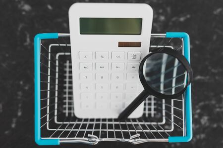 consumerism and budgeting conceptual still-life, shopping basket with magnifying glass and calculator in itの写真素材