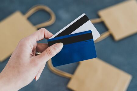 shopping and consumerism conceptual still-life, hand holding payment cards in front of the camera with shopping bags bokeh in the backgroundの写真素材