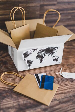 online shopping and international deliveries conceptual still-life, parcel with world map and shopping bags inside next to payment cardsの写真素材