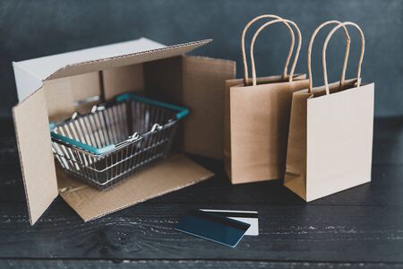 online shopping conceptual still-life, parcel with shopping basket and bags next to it with gift cards or payment cardsの写真素材