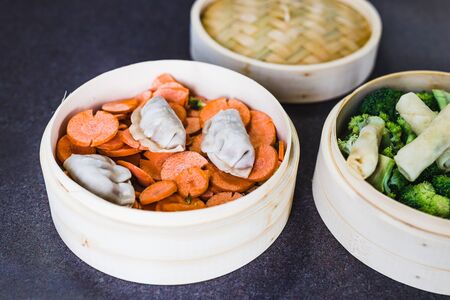healthy plant-based meal concept, veggies with spring rolls and dumplings in bamboo steamer for...