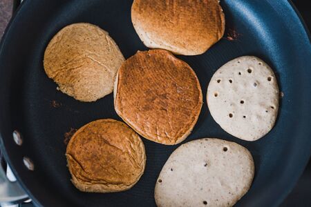 healthy plant-based recipes concept, vegan banana pancakes cooking in a pan with some already flipped other just pouredの写真素材