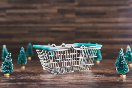 Shopping basket surrounded by miniature Christmas trees, concept of festive season shoppingの写真素材