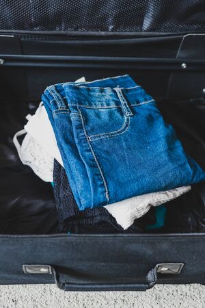 travel essentials and packing for a holiday concept, luggage with pile of clothes insideの写真素材