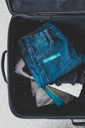 travel essentials for a holiday, luggage with pile of clothes and Packing Everything label on them