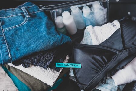 travel essentials for a holiday, luggage with pile of clothes and Packing Everything label on themの写真素材