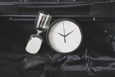 time to travel or delay during a trip conceptual still-life, empty suitcase with clock and hourglass...