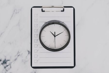 concept of schedules and productivity, to do list on clipboard next to clock on business deskの写真素材