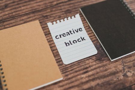 creative block or writer's block conceptual still-life, notepads on wooden desk with text doodle on...