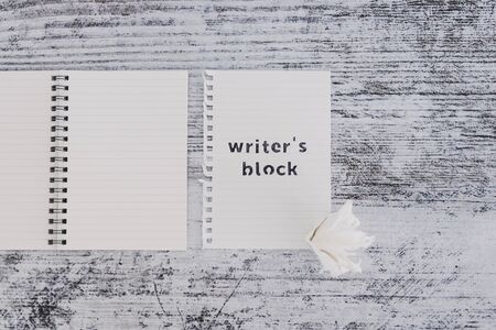 creative block or lack of inspiration conceptual still-life, piece of paper on wooden desk with Writer's Block text surrounded by blank notepads and with scrunched paper ball next to itの写真素材