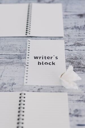 creative block or lack of inspiration conceptual still-life, piece of paper on wooden desk with Writer's Block text surrounded by blank notepads and with scrunched paper ball next to itの写真素材