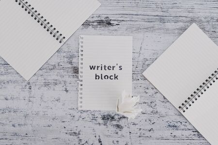 creative block or lack of inspiration conceptual still-life, piece of paper on wooden desk with Writer's Block text surrounded by blank notepads and with scrunched paper ball next to itの写真素材
