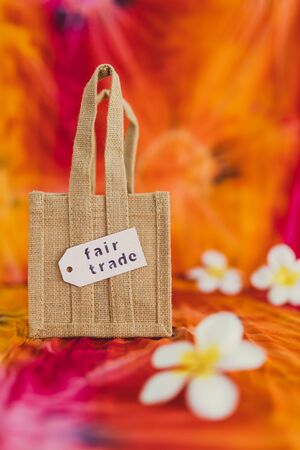 ethical shopping and locally sourced items conceptual still-life, small canvas bag made of natural materials with Fair Trade text on price tag on hippie tie dye backgroundの写真素材