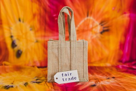ethical shopping and locally sourced items conceptual still-life, small canvas bag made of natural materials with Fair Trade text on price tag on hippie tie dye backgroundの写真素材