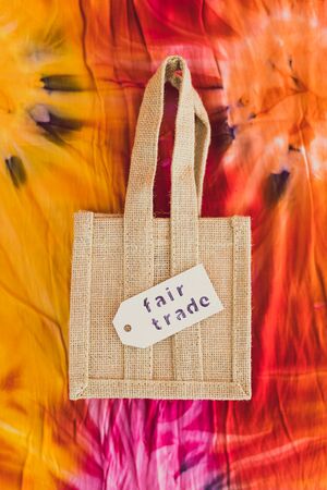 ethical shopping and locally sourced items conceptual still-life, small canvas bag made of natural materials with Fair Trade text on price tag on hippie tie dye backgroundの写真素材
