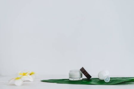 vegan natural beauty without harsh chemicals concept, pot of face cream and bottle of body lotion on tropical green leaf with monoi flowersの写真素材