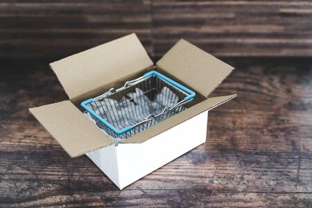 concept of home delivery of groceries and online shopping, open parcel with shopping basket inside of itの写真素材