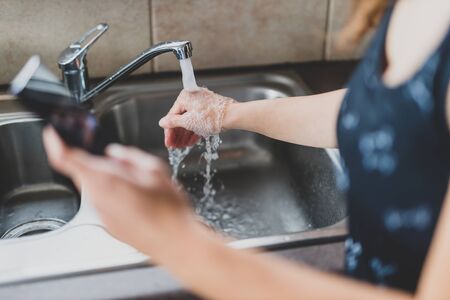 flattening the curve through hygiene against pandemic outbreaks like covid-19, woman washing her hands while scrolling social media or news on her smartphone in self-isolationの写真素材