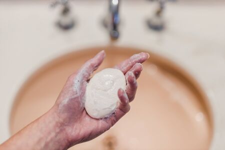 flattening the curve through hygiene against pandemic outbreaks like covid-19, woman washing her hands in the bathroom holidng soap bar shot at shallow depth of fieldの写真素材