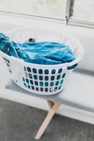 routines and life at home concept, laundry basket iwth mixed clothes on a bench next to window light shot at shallow depth of fieldの写真素材