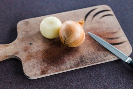 healthy food ingredients and organic produce concept, onions on cutting board with knife one alrey peeled and one with skin onの写真素材