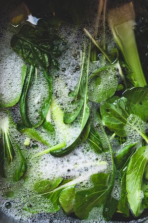 healthy plant-based food ingredients concept, mixed green leaves including celery and bok choy getting washined in kitchen sinkの写真素材