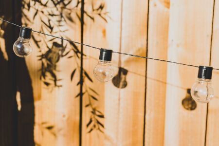 string lights with lightbulb shape and tree branches shadows on wooden fence in backyardの写真素材