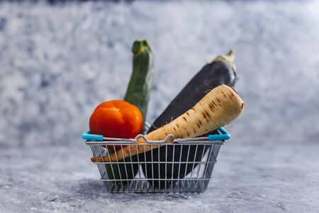 healthy plant-based food ingredients concept, zucchini eggplant tomato and parsnip in grocery shopping basketの写真素材