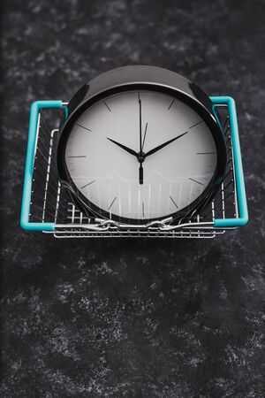 concept of flash sales and time limited marketing offers, big clock inside grocery shopping basket on dark backgroundの写真素材